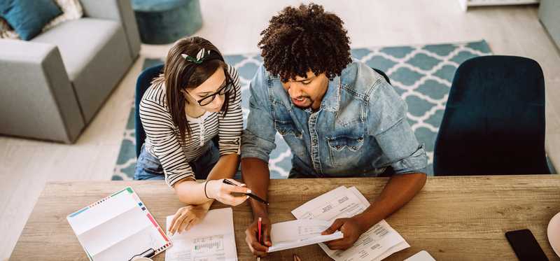 Two people review bills at table in living room.