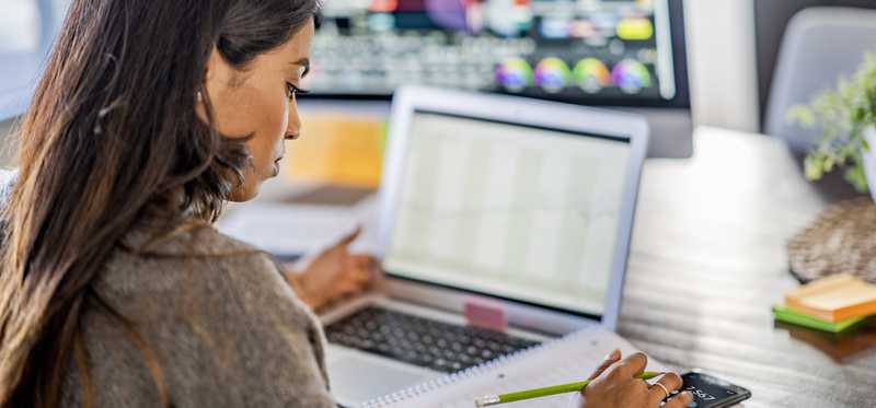 Investor uses calculator while looking at laptop screen.