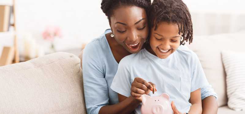 Adult holding child and putting coin in piggybank.