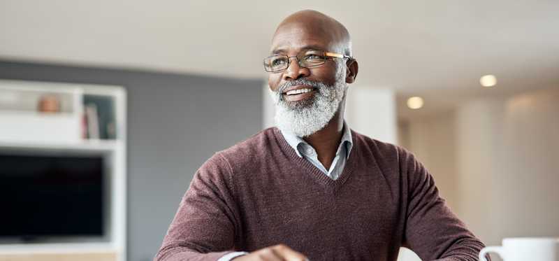 Person sitting at home smiles while holding paperwork on tabletop.