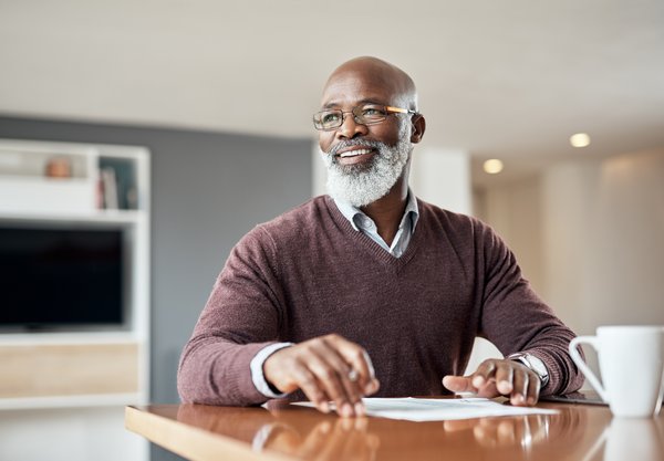 Person sitting at home smiles while holding paperwork on tabletop.