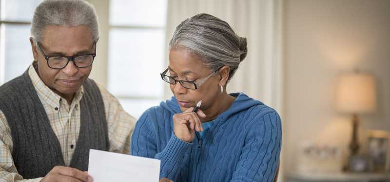 Two people carefully review paperwork at dining table.