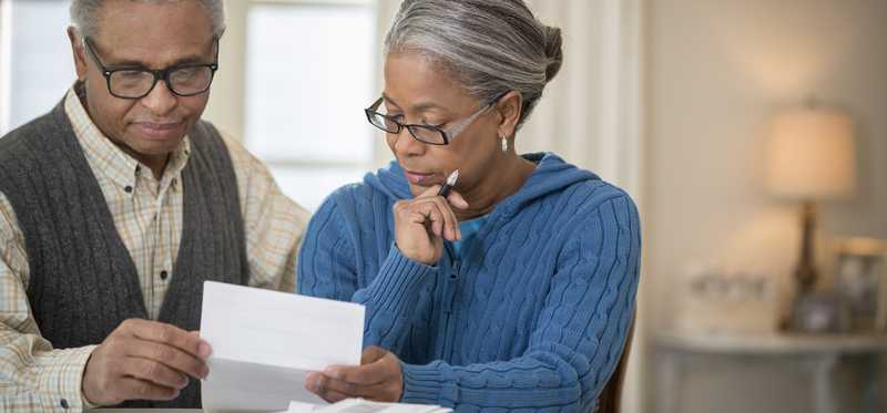 Two people review paperwork at table in home.