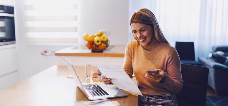 Person smiling while holding phone and looking at document.