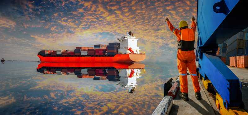 A freighter pulling into a dock with a dock worker guiding it.