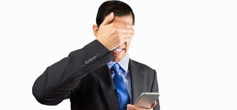 Person in suit covering eyes with one hand and holding phone in other.