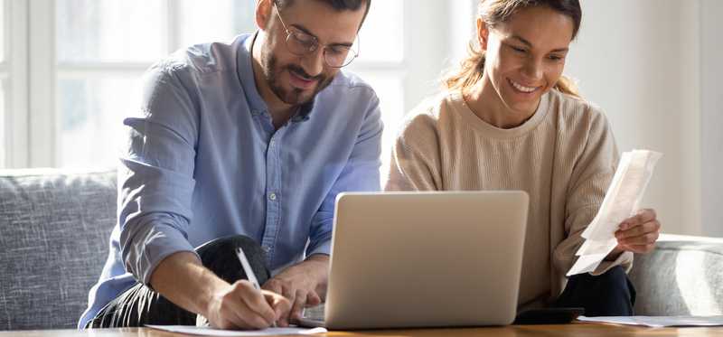 Smiling couple using laptop and taking notes