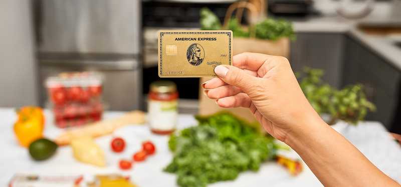 Person holding up an American Express card inside a kitchen.
