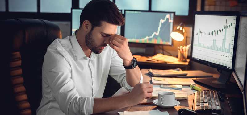 Frustrated investor with hand on face and looking down.
