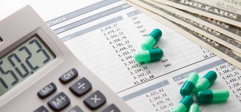 Green pills next to calculator on financial paperwork.