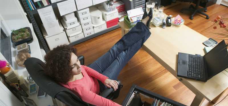 Person with feet on office desk is looking through file cabinet.