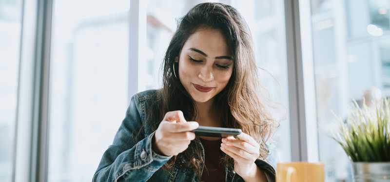 Young woman smiles while looking at her phone.