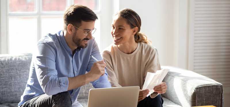 Two people sitting on couch smile while they review receipts.