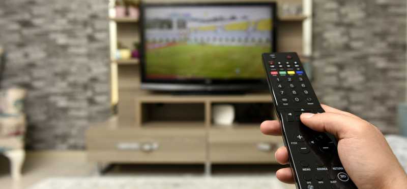 Hand holding remote in front of TV.