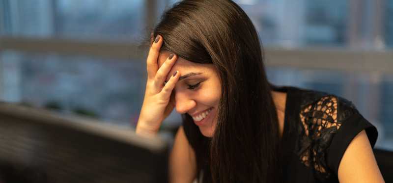 Person smiling at laptop while putting hand to forehead.