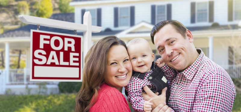 Smiling family in front of house with For Sale sign