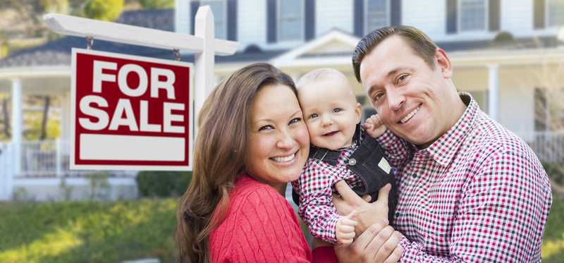 Smiling family in front of a house with a For Sale sign.