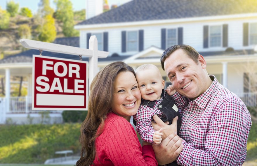 Smiling family in front of a house with a For Sale sign.