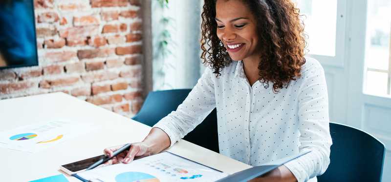 Smiling person holding folder with charts inside at table.