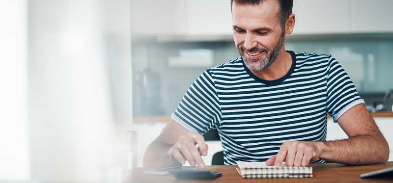 Person using calculator and notepad in kitchen.