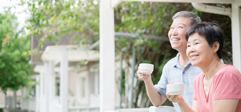 Two people smiling and holding tea cups on a porch.