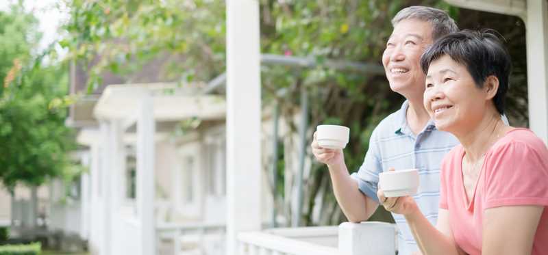 Two people smiling and holding cups on porch.