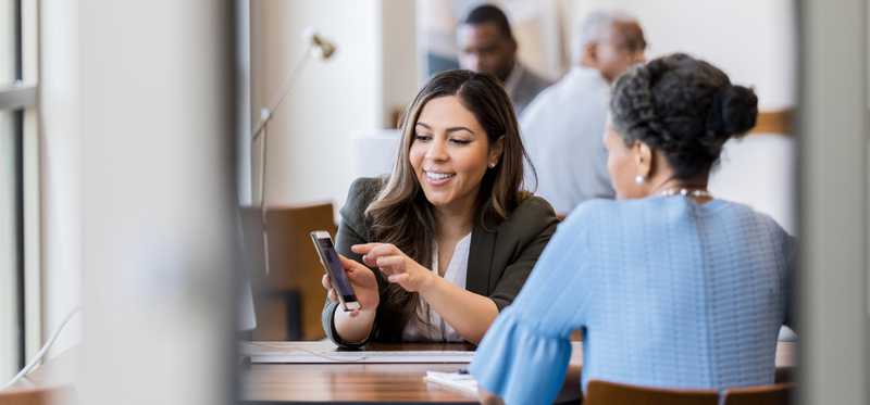 Two people sitting in an office and looking at a phone.