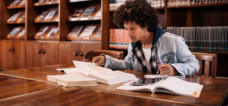 A young male with books open at the library.