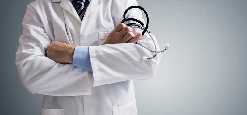 A doctor standing in his white coat with arms crossed.
