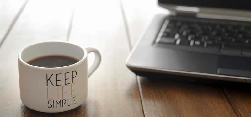 Coffee mug that says Keep Life Simple sitting on a desk near a laptop.