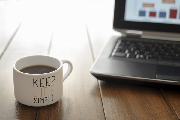 Coffee mug that says Keep Life Simple sitting on a desk near a laptop.