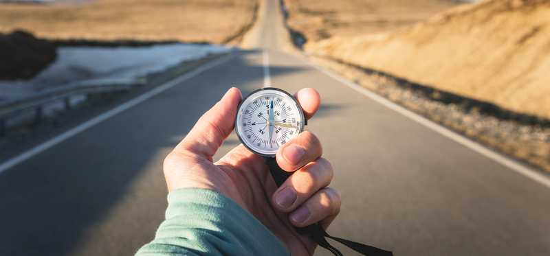 Person holding a compass in the middle of a desert highway.