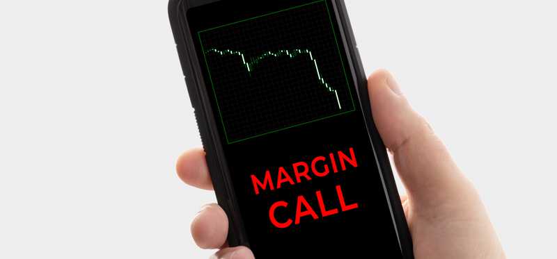 Hand holding phone displaying stock down graph and the words Margin Call