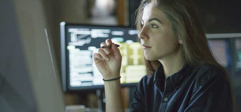 Woman holding pen and looking at computer