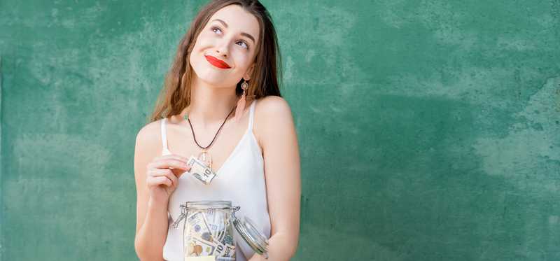 Woman inserting cash into jar labeled Dream