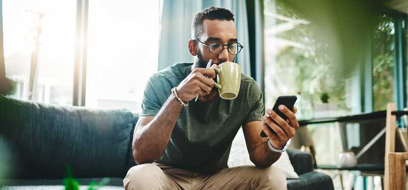 Person drinking out of coffee mug and checking phone while reviewing paperwork.