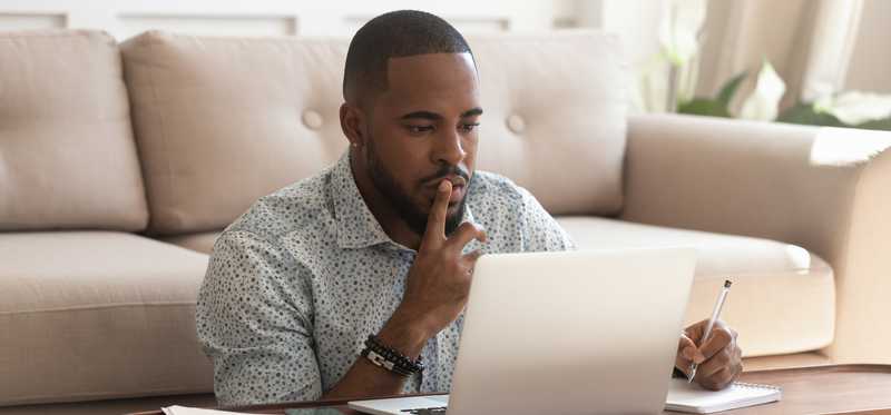 Person sitting on floor with laptop on coffee table and holding finger to their lips.