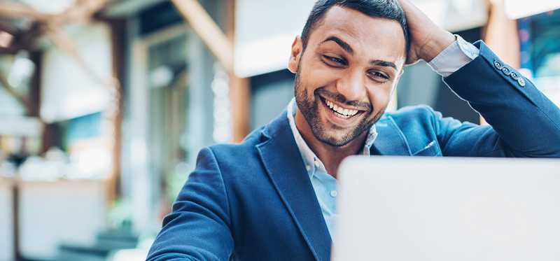 Person smiles and scratches head while looking at laptop.