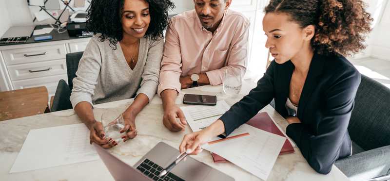 Three people meeting around table and looking at laptop.