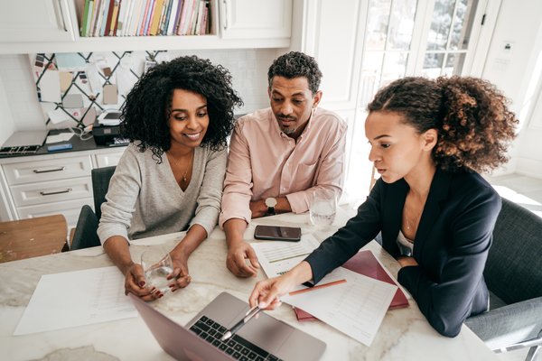 Three people meeting around table and looking at laptop.