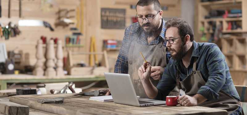 Two men looking at a laptop screen in a workshop.