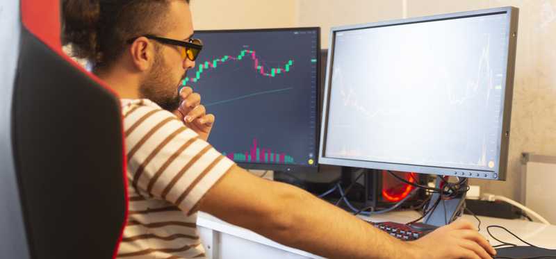 Casually dressed investor looking at two screens.