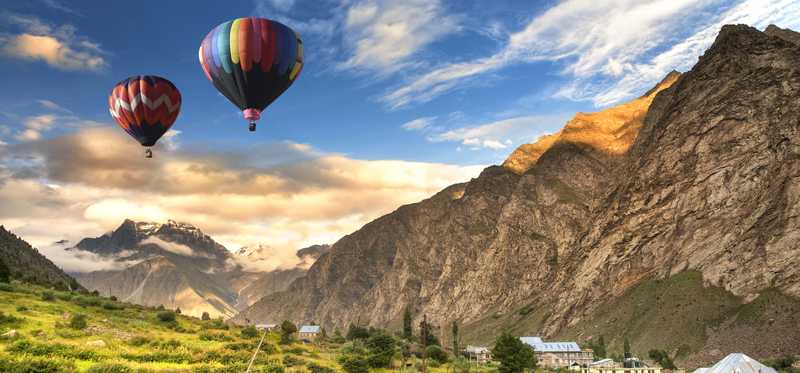 Hot air balloons flying over a grassy field with mountains in the background.