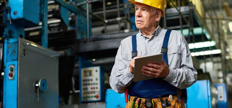 Older man in a hardhat with a clipboard.