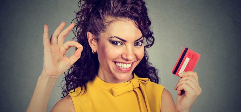 Smiling woman holding a credit card and giving the okay sign.