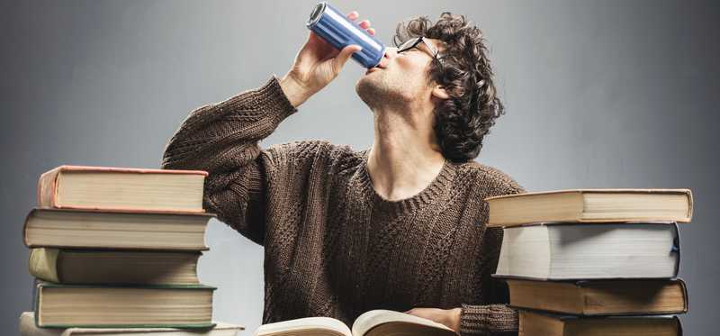 Person drinking from a can in the middle of stacks of books