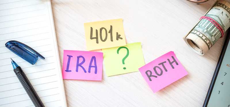 Sticky notes with 401k, IRA, Roth, and a question mark on a desktop.