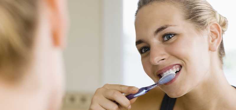 Woman brushing her teeth in a mirror