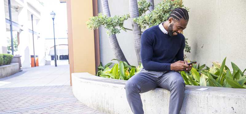Person depositing paycheck while sitting on wall outside.