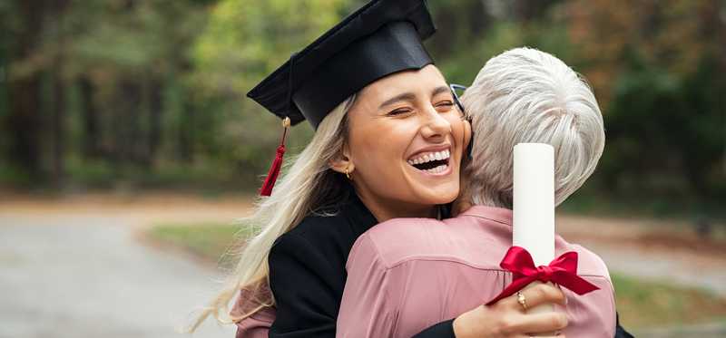 A person wearing a graduation cap and gown embraces another person.
